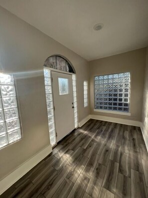 A hallway with a wooden floor, a door with a window, and a window with a grid pattern. - Historic University 3BR  (Tucson)