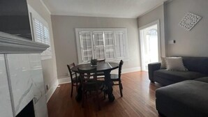 A living room with a dark grey sofa, a dining table with chairs, and a window with shutters. - Historic University 3BR  (Tucson)
