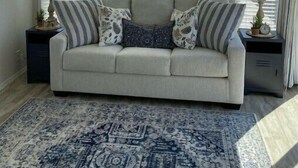 A living room with a sofa, patterned pillows, a blue rug, and a ceiling fan.