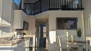 A modern kitchen with white cabinets, a black railing, and a dining area with wooden chairs.