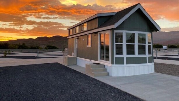 A modern house with a large windowed porch, a small attached garage, and a view of the mountains at sunset.