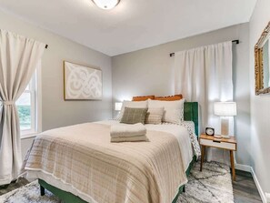 Une chambre à coucher avec un lit, des rideaux, une table de chevet avec une lampe et un tableau encadré au mur.