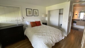 A bedroom with a bed, a dresser, a nightstand, a lamp, a door, and a mirror. - Peaceful View Home with a Cozy Modern feel walking distance to the beach (Seattle)