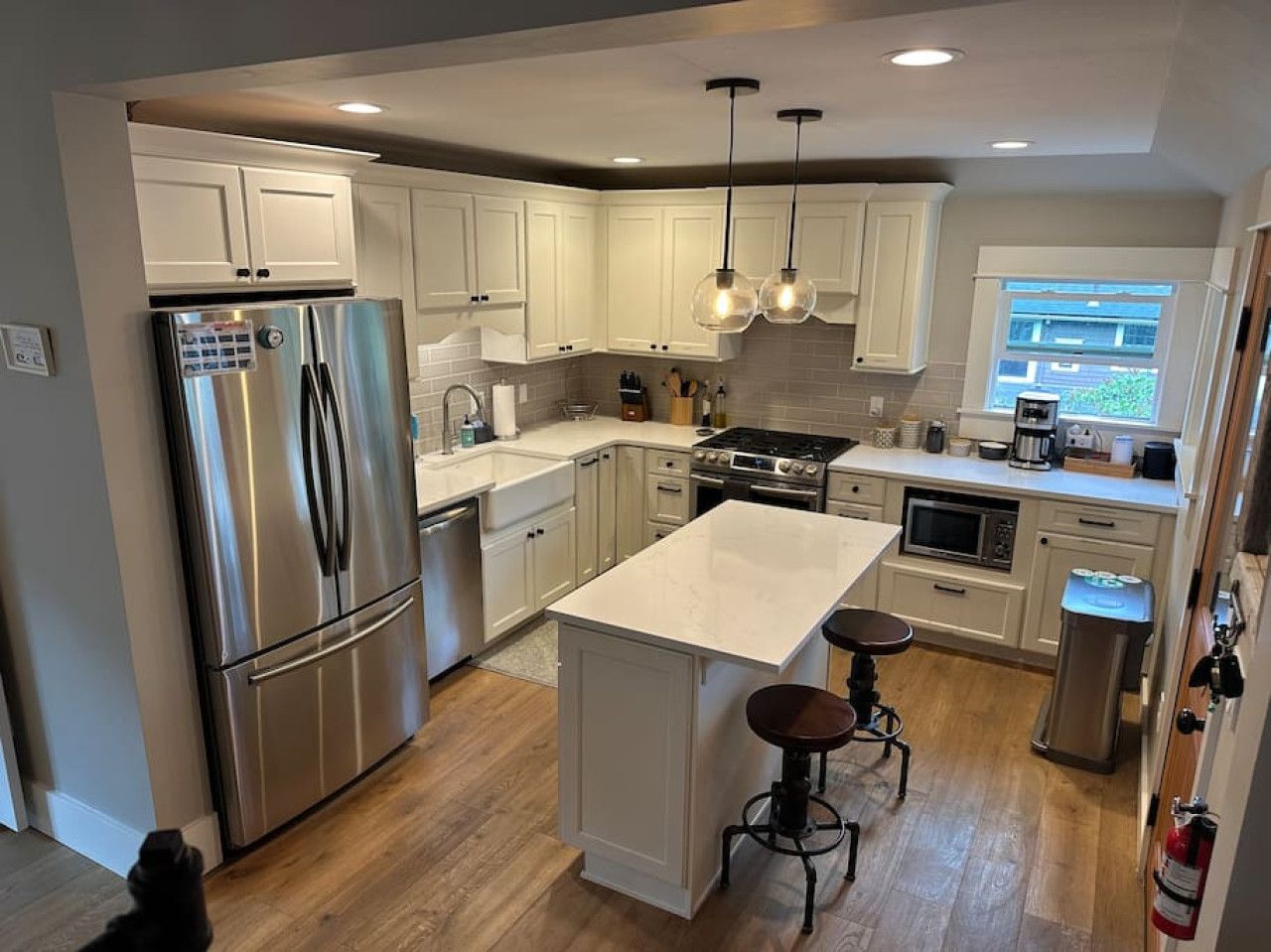 A modern kitchen with stainless steel appliances, white cabinetry, a central island with stools, and pendant lighting.