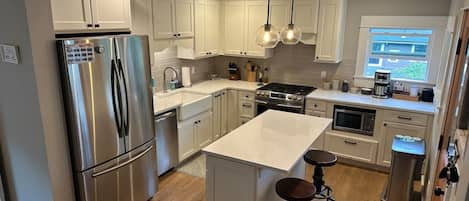A modern kitchen with stainless steel appliances, white cabinetry, a central island with stools, and pendant lighting.