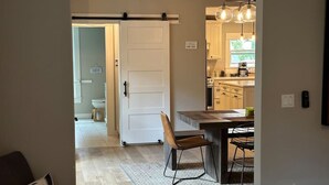 Una cocina moderna con comedor, una puerta corredera que da a un baño y un enchufe visible en la pared.