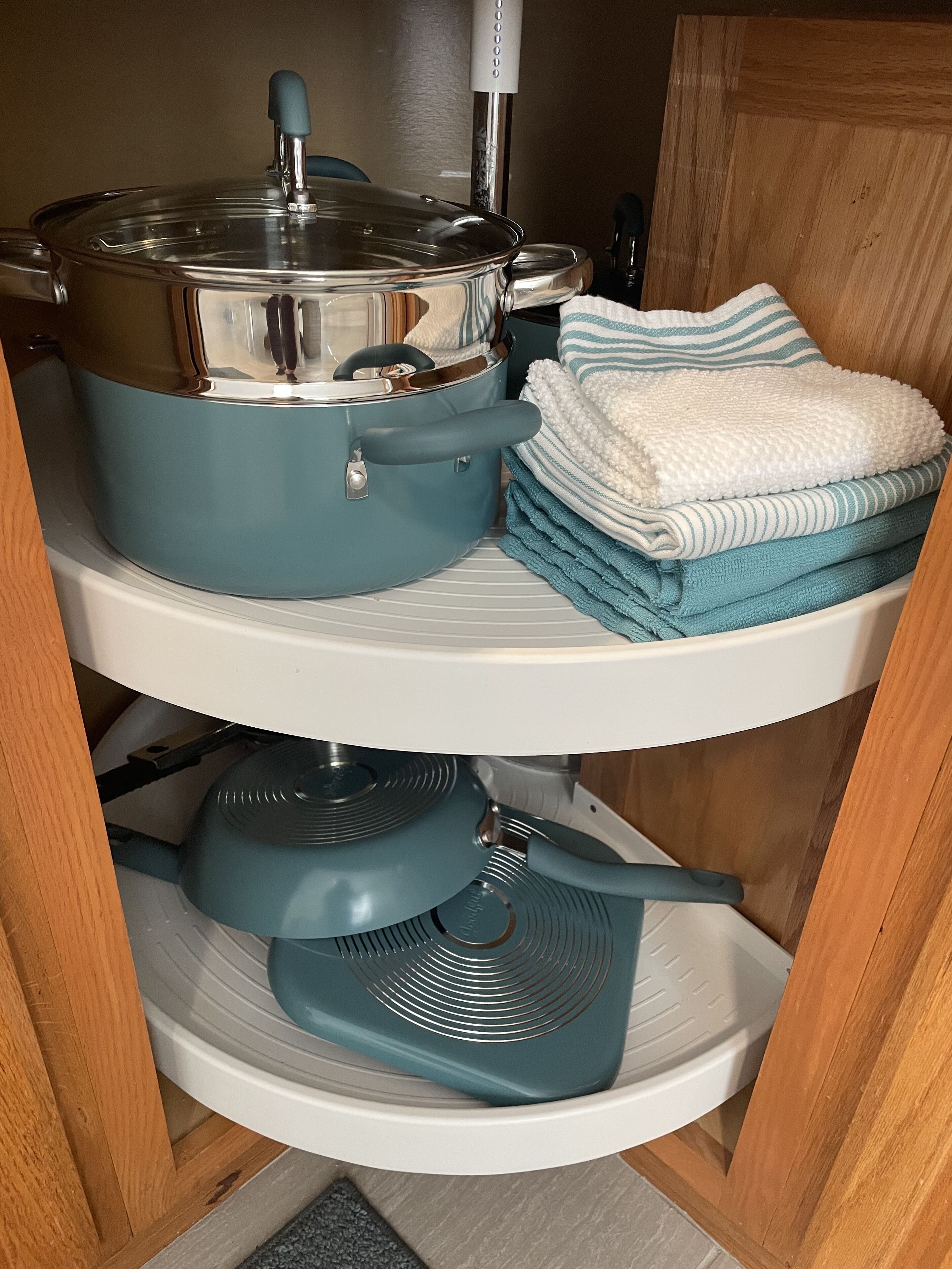 Une cuisine avec une casserole bleue sur l’étagère supérieure, une casserole blanche sur l’étagère du milieu et une poêle bleue sur l’étagère inférieure. Des serviettes pliées, dans des tons de bleu et de blanc, se trouvent sur l’étagère supérieure.