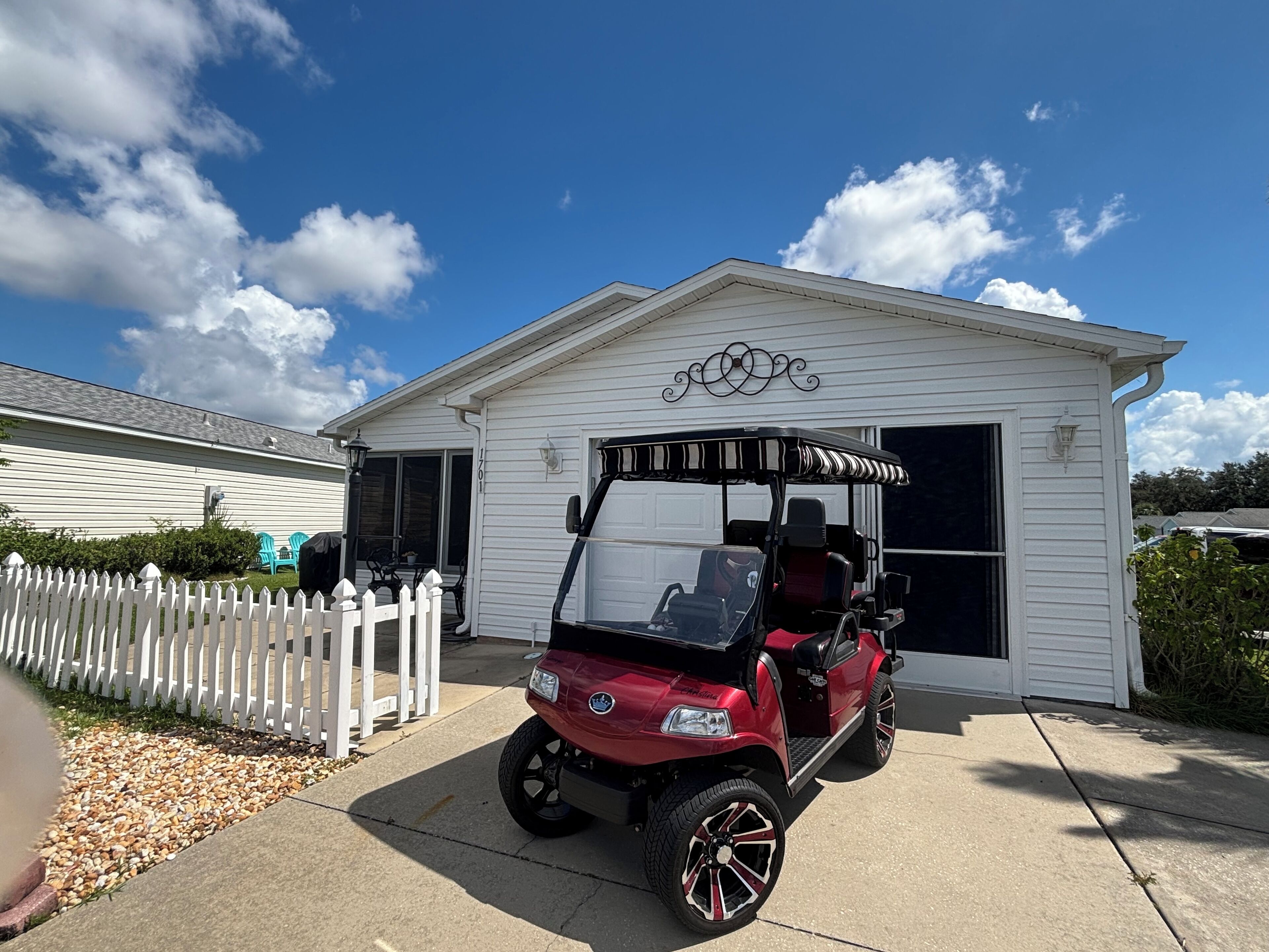 A red golf cart parked in front of a white garage with a decorative awning.