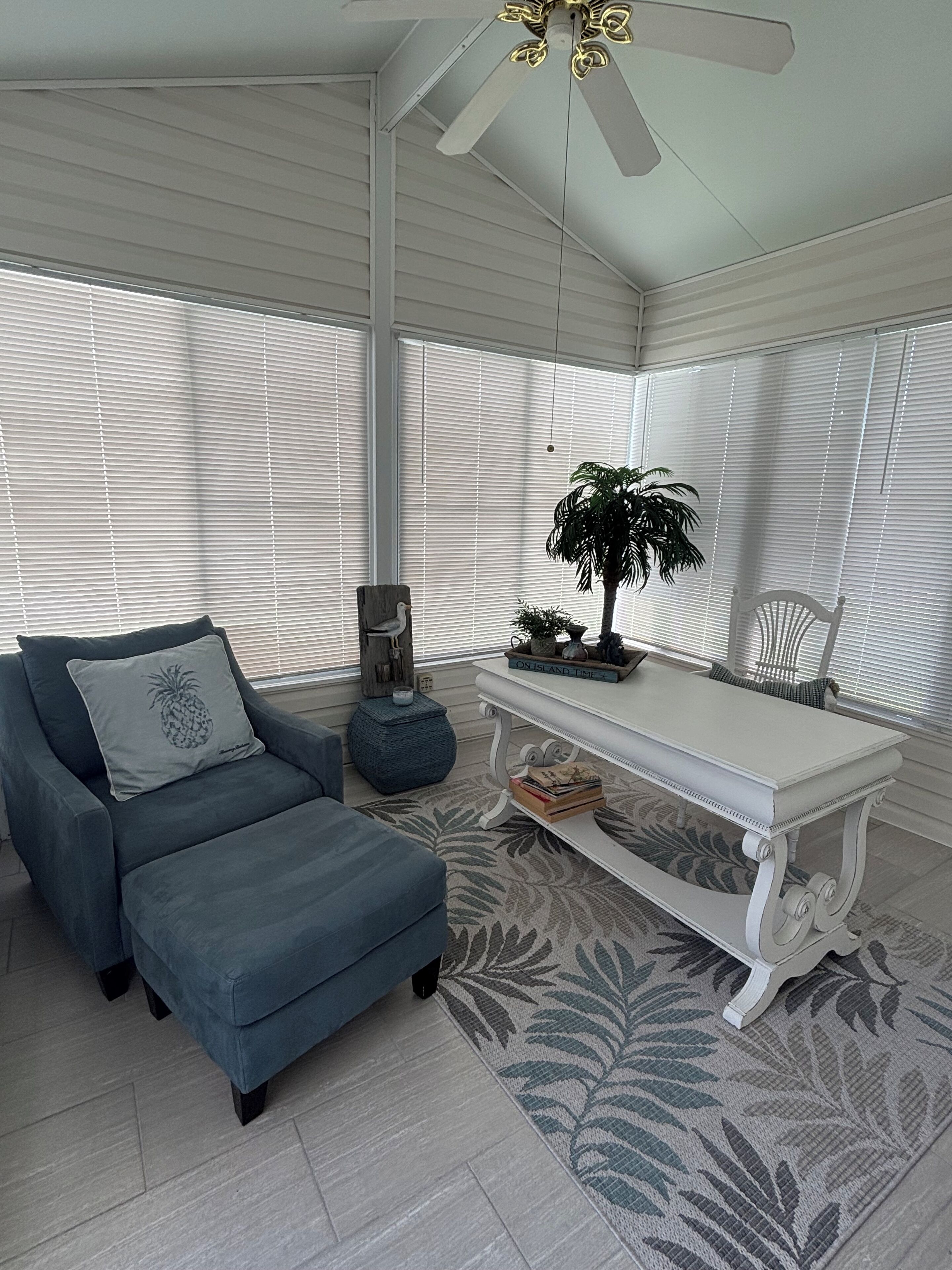 A room with a grey sofa, a white table, and a ceiling fan.
