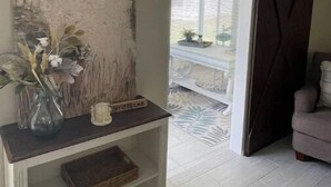Ein Wohnzimmer mit einem großen abstrakten Gemälde, einer Vase mit getrockneten Blumen, einer kleinen Holzskulptur und einer Schiebetür, die auf einen Balkon führt.