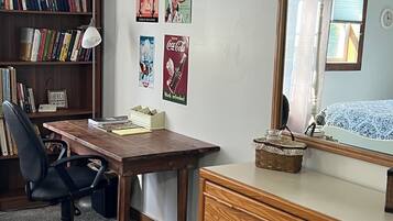 A room with a wooden desk, a chair, a dresser, a bookshelf, and wall decorations including posters.