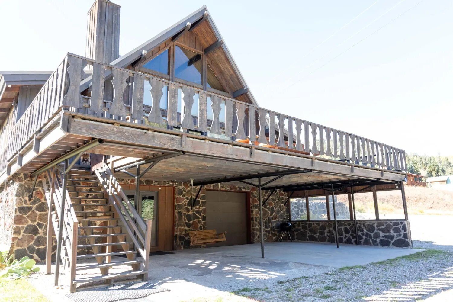A two-story log cabin with a balcony, stone exterior, and a covered outdoor area with a grill.