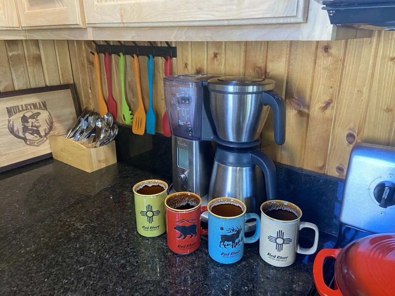 A kitchen counter with a coffee maker, mugs, and utensils.