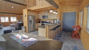 A spacious kitchen with wooden cabinets, a central island with stools, a microwave, and a refrigerator. - "Peace Like a River" mountain cabin on river - Red River, NM. Hot tub optional. (Red River)