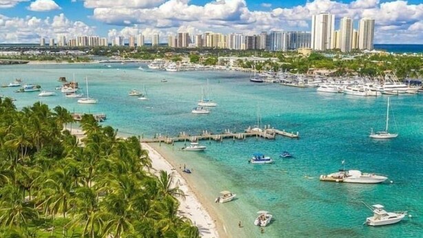Un paisaje urbano costero con una playa, aguas turquesas cristalinas y numerosos barcos.