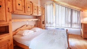 Un dormitorio de madera con cama, armarios empotrados y ventana con cortinas.