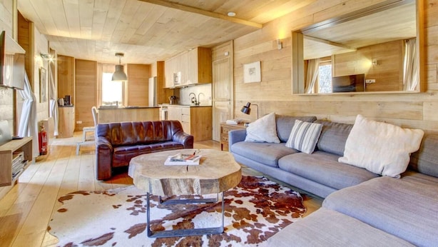 A cozy cabin interior with a wooden ceiling, a living area with a sofa and a coffee table, a kitchen area, and a large mirror on the wall. - 1st floor, terrace, balcony, fireplace or stove, tv, ski locker, 82m², Morzine (Morzine)