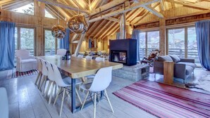 Un salón amplio con techo de madera, chimenea de piedra y una gran mesa de comedor con sillas.