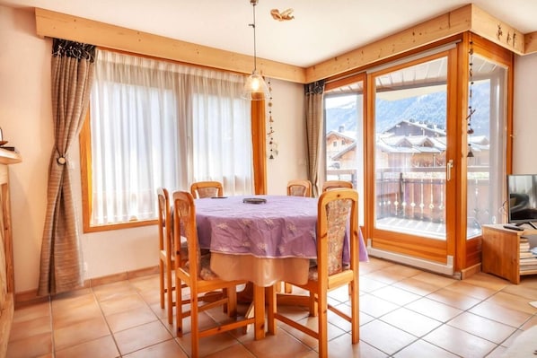 A dining area with a table set for four, wooden chairs, a purple tablecloth, and a view of a mountain landscape through a large sliding glass door.