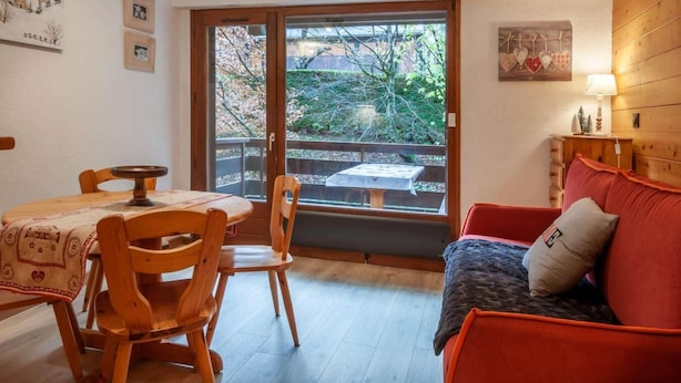 A cozy room with a wooden dining table, chairs, a red sofa, and a sliding glass door leading to an outdoor patio. - 1st floor, balcony, tv, ski locker, 25m², Morzine (Morzine)