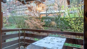 A balcony with a table and chairs, overlooking a garden with various plants and a building in the background. - 1st floor, balcony, tv, ski locker, 25m², Morzine (Morzine)