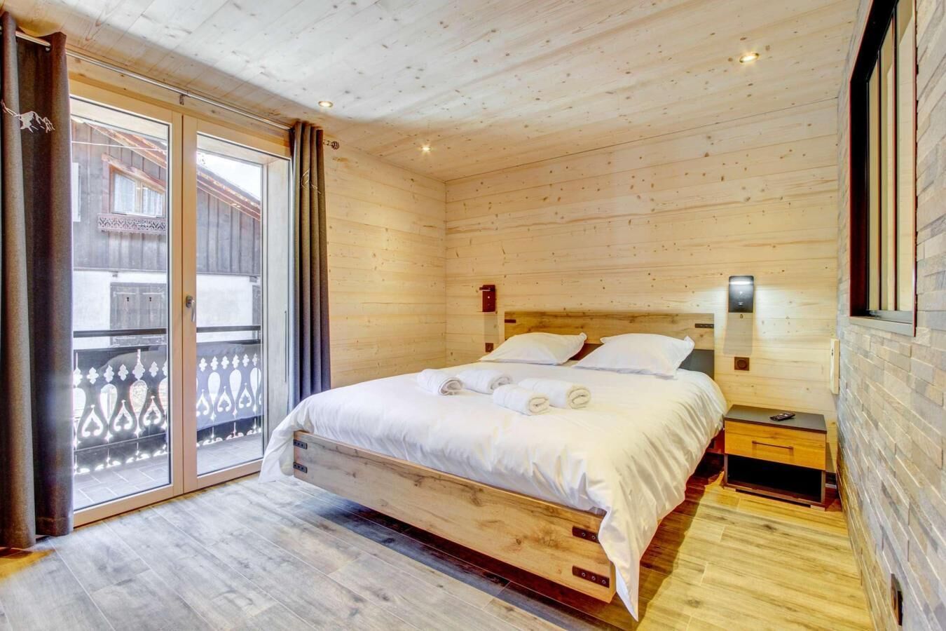 A wooden cabin bedroom with a bed, a nightstand, and a sliding glass door to a balcony.