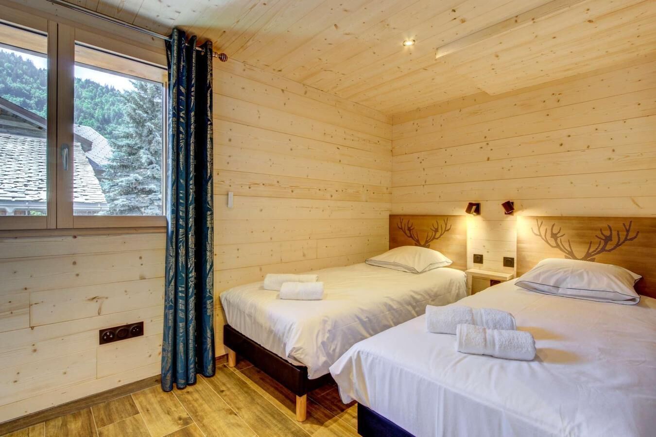 Una habitación de cabaña de madera con dos camas, una ventana con cortinas y un cabecero con diseño de asta de ciervo.