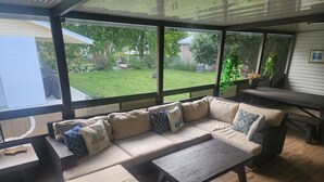 Un patio cubierto con un sofá seccional color beige, una mesa de centro de madera y una mesa de comedor.