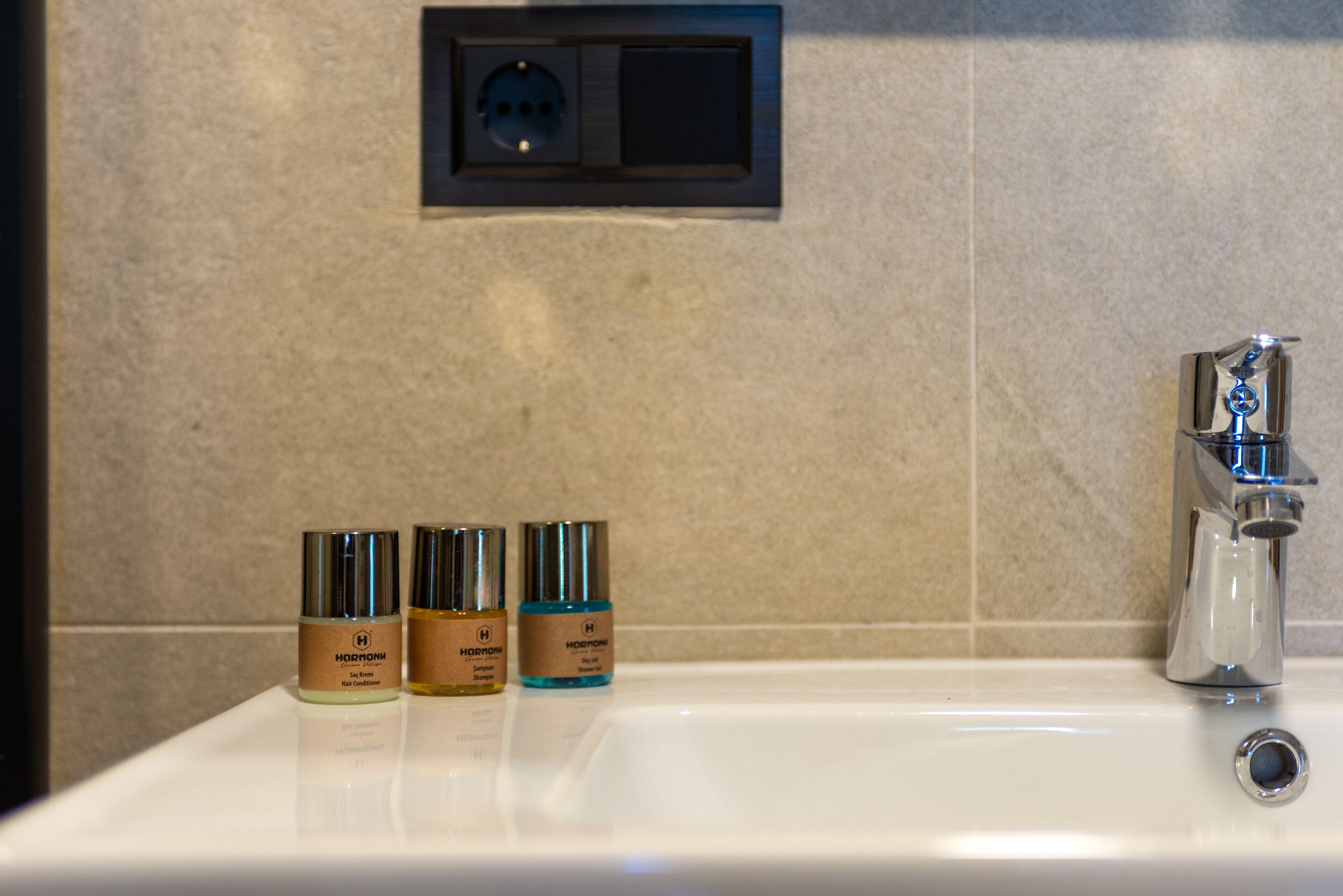 A bathroom sink with three bottles of HORMONE body lotion.
