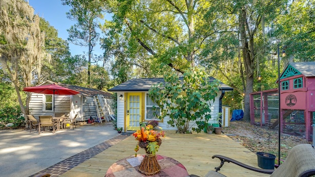 A wooden deck with a table and chairs, a small house with a yellow door, and a pink building with a tree design. - Wilmington Area Studio ~ 4 Mi to Downtown! (Leland)
