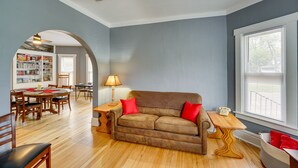 Una sala de estar con un sofá marrón, cojines rojos, una mesa de centro de madera, una lámpara y una estantería.