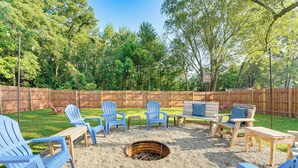Un patio trasero con una fogata, sillas Adirondack azules y una mesa de madera.