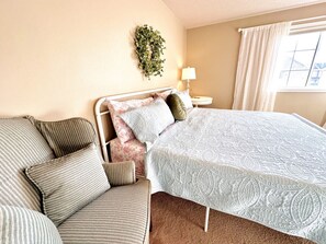 A bedroom with a bed, a sofa, a nightstand, a lamp, and a window with curtains.