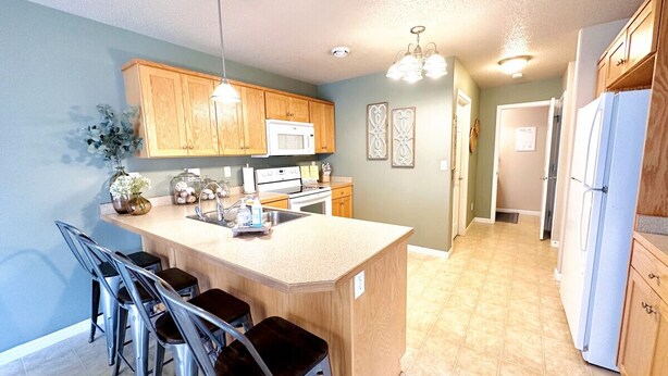 A kitchen with wooden cabinets, a central island with bar stools, a microwave, and a refrigerator. - Westport Beach Hideout (West Fargo)