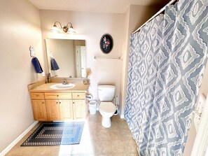 A bathroom with a wooden vanity, a toilet, a mirror, a towel rack, and a patterned shower curtain.