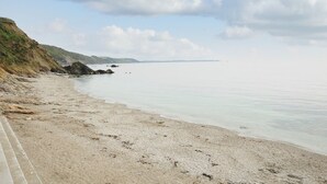 A coastal beach with a sandy shore, a rocky outcrop, and a clear sky. - Little Trevallan (Looe)