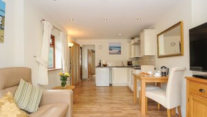 A modern apartment with a living room, dining area, and kitchen. There is a sofa, a dining table, and a TV. - Little Trevallan (Looe)