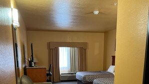 Une chambre d’hôtel comprenant un lit, un bureau, une chaise, un petit canapé, une fenêtre avec des rideaux et un luminaire au plafond.