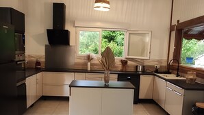 A modern kitchen with a central island, a built-in oven, and a window providing a view of greenery outside.