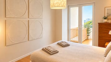 Ein Schlafzimmer mit einem großen Bett, einem runden Wandbild, einer Deckenleuchte und Blick durch eine Schiebetür.