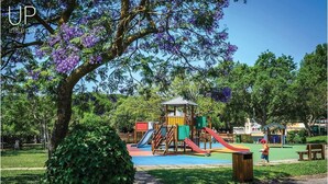 Un parque infantil con toboganes y estructuras para escalar, rodeado de árboles y un cielo despejado.