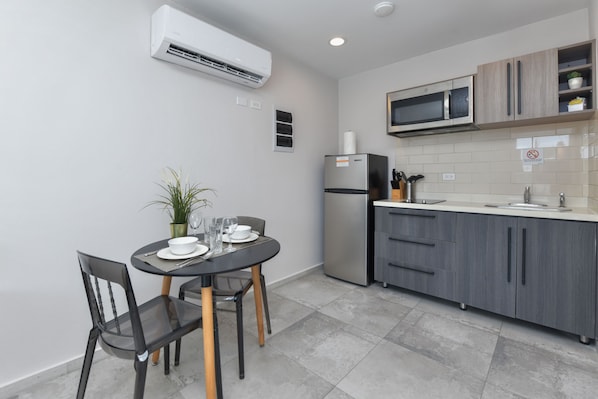 Cozinha compacta com mesa, cadeiras, geladeira, micro-ondas e uma planta em vaso.