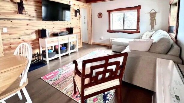 A cozy cabin-style room with a wooden interior, a sofa, a television, and a dining area with a table and chairs. - NEW - Apache Cabin (Heber-Overgaard)