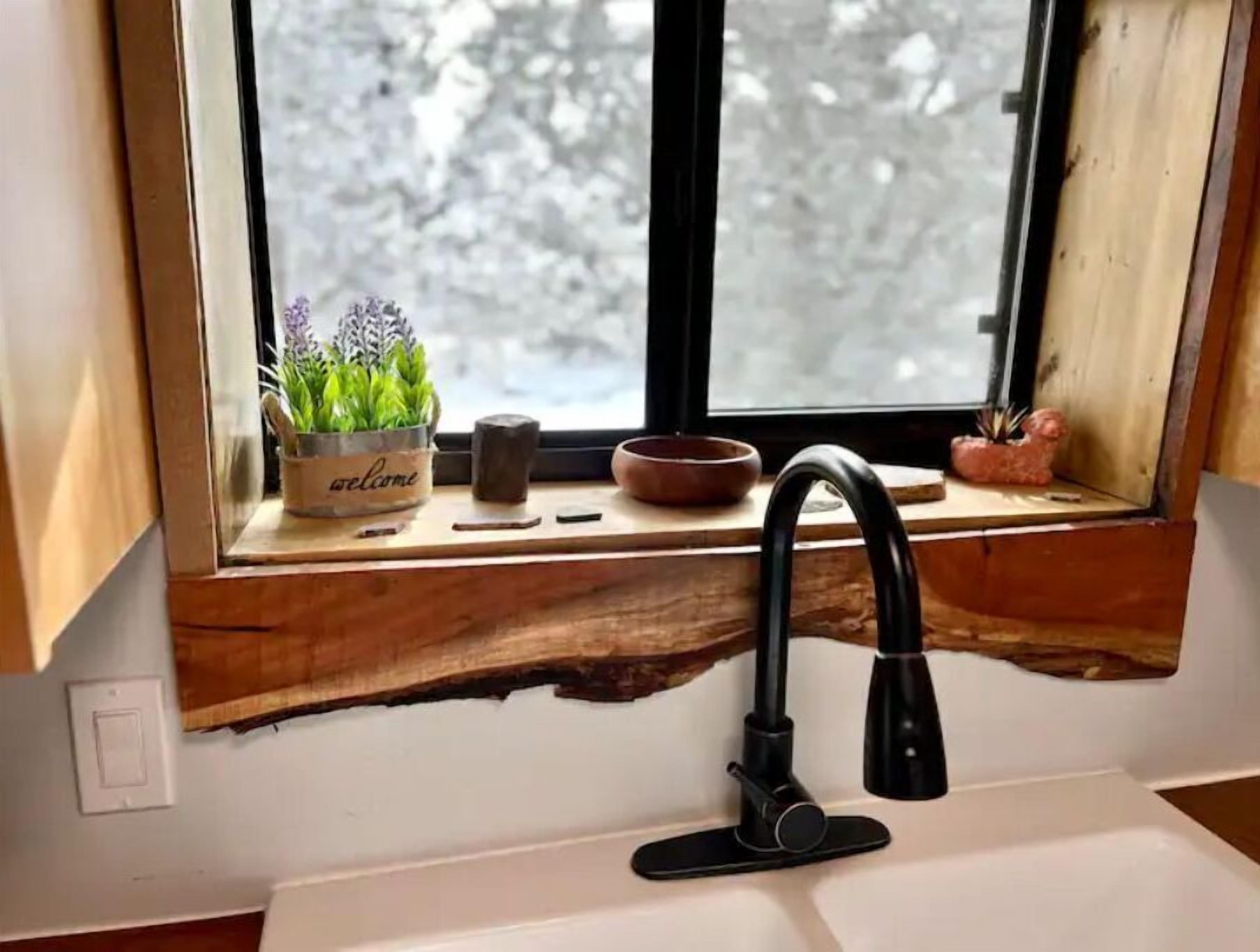 A kitchen sink with a black faucet, a wooden window sill, and a window with a view of snow-covered trees.