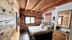 A wooden cabin bedroom with a bed, dresser, and a window. - NEW - Apache Cabin (Heber-Overgaard)