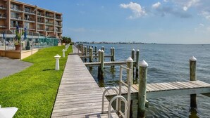 A wooden pier extending into calm water, with a grassy area and a multi-story building on the left. - Ocean City Bayfront Ponte Vista (Ocean City)