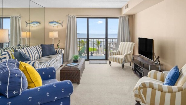 A living room with striped sofas, a television, and a view of the ocean. - Ocean City Bayfront Ponte Vista (Ocean City)