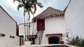 A swimming pool with a stone border, a thatched-roof building, and palm trees. - Complimentary 1 hr Massage in our Traditional Open-Air Palapa w/ Private Pool (Sayulita)