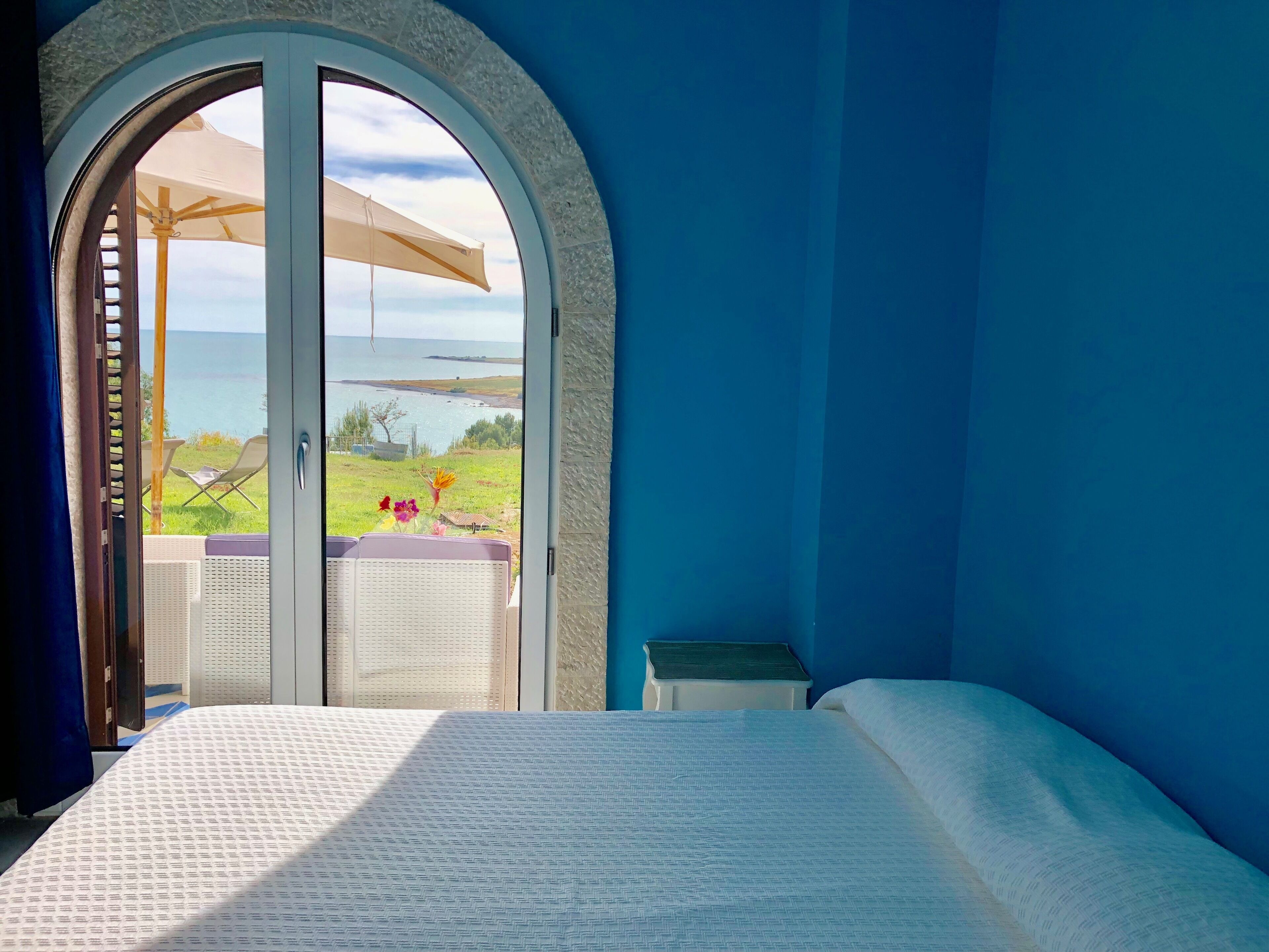 Ein Schlafzimmer mit einem großen Bogenfenster, das auf eine Wiese und ein Gewässer blickt.