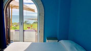Ein Schlafzimmer mit einem großen Bogenfenster, das auf eine Wiese und ein Gewässer blickt.